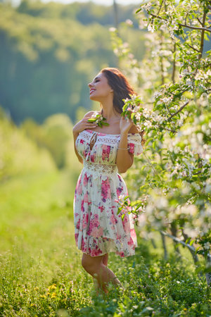Full body portrait of a beautiful woman in a dress in a blooming apple orchard on a sunny spring dayの写真素材