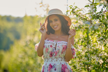 portrait of a beautiful woman in a dress in a blooming apple orchard enjoying a sunny spring dayの写真素材