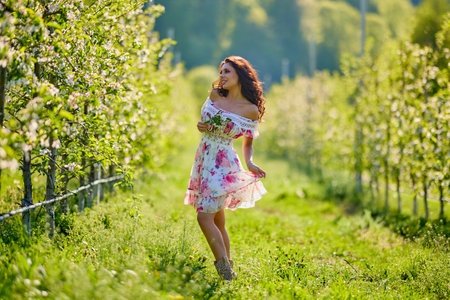 Full body portrait of a beautiful woman in a dress in a blooming apple orchard on a sunny spring dayの写真素材