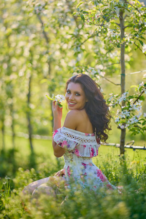 portrait of a beautiful woman in a dress in a blooming apple orchard enjoying a sunny spring dayの写真素材