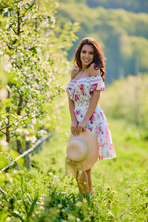 Full body portrait of a beautiful woman in a dress in a blooming apple orchard on a sunny spring dayの写真素材