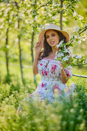 portrait of a beautiful woman in a dress in a blooming apple orchard enjoying a sunny spring dayの写真素材