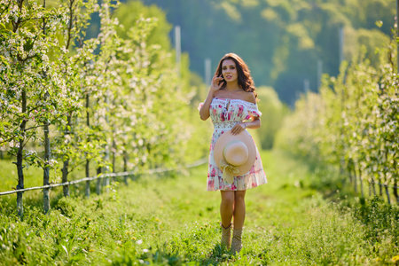 Full body portrait of a beautiful woman in a dress in a blooming apple orchard on a sunny spring dayの写真素材