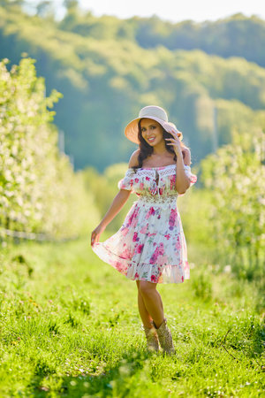 Full body portrait of a woman in a dress in a blooming apple orchard on a sunny spring dayの写真素材