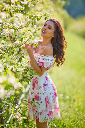 portrait of a beautiful woman in a dress in a blooming apple orchard enjoying a sunny spring dayの写真素材