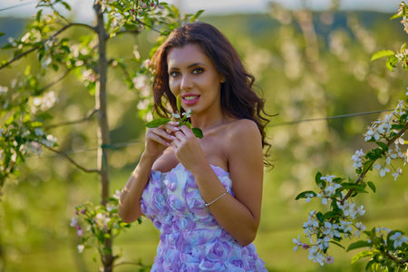portrait of a beautiful woman in a dress in a blooming apple orchard with a blurred backgroundの写真素材