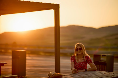 portrait of a woman sitting on a bench and relaxing with sunset in the backgroundの写真素材