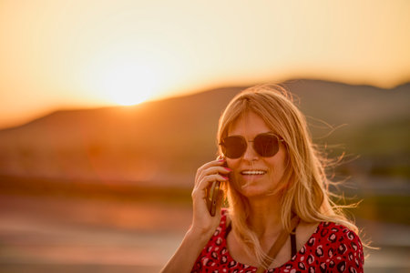 portrait of a woman talking on the phone and smiling with sunset in the backgroundの写真素材