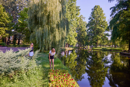 Two middle-aged sisters spending a summer morning in the park by a lake relaxing and having fun.の写真素材