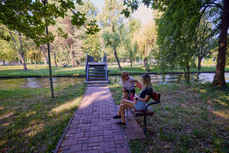 Two middle-aged sisters spending a summer morning in the park by a lake relaxing and having fun.の写真素材