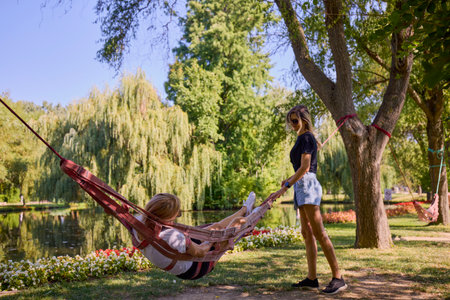Two middle-aged sisters spending a summer morning in the park by a lake relaxing and having fun.の写真素材