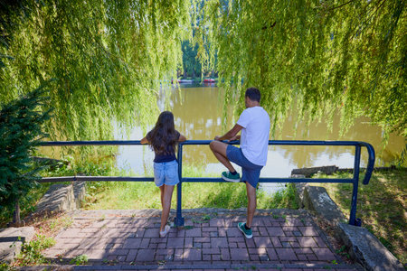 Father and daughter in the park by a lake on a summer morning spending time together enjoying...