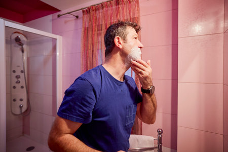 middle-aged man in the bathroom in the morning brushing his teeth, shaving and styling his hairの写真素材