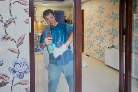 Middle-aged man cleans the house with a vacuum cleaner, dusts and mops the floorの写真素材