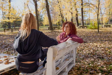 A middle-aged woman in the park with her friend is relaxing, chatting and having a snack.の写真素材