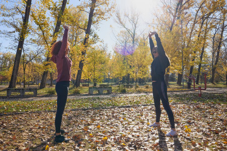 A middle-aged woman in the park with her friend doing sports together on a beautiful autumn day