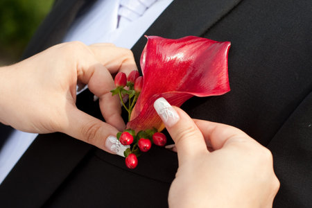 Bride arranging boutonniere flower on suit jacke groom