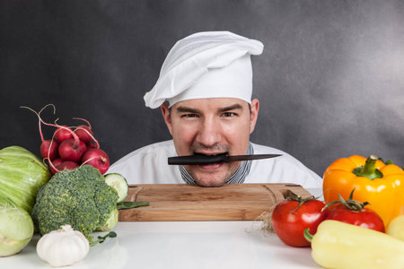 Funny young chef with knife and vegetable on black の写真素材