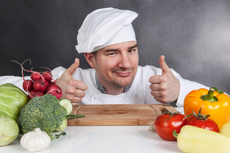 Young chef with OK sign and vegetable on black の写真素材