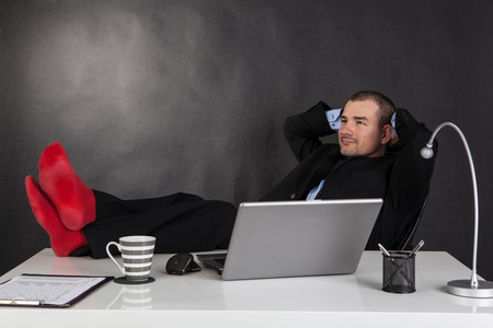 Smiling businessman relaxing with feet over up his deskの写真素材
