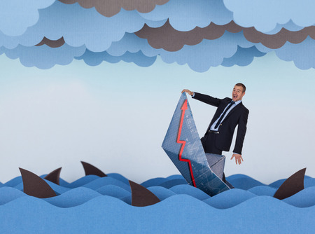 Businessman and paper boat is sinking into paper sea. Paper waves, clouds, boat and sharks.の写真素材