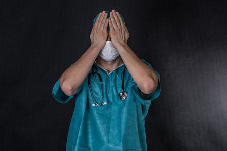 Surgeon in scrubs covering eyes. Black background