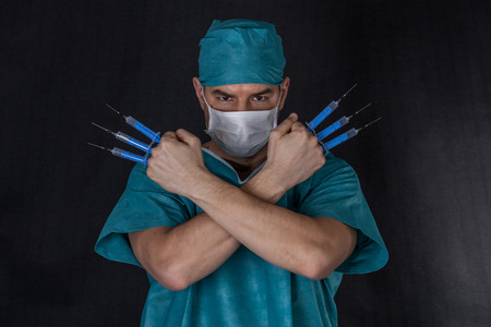 Surgeon in scrubs with syringes arms crossed on a black backgroundの写真素材