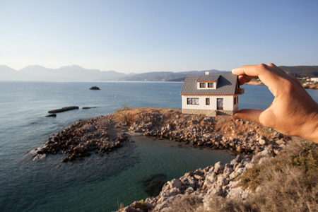 Dream to have a house. Hand holding a model house on the beachの写真素材