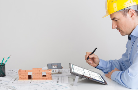Architect using digital tablet on office table desk. Model house construction with brick on blueprintの写真素材