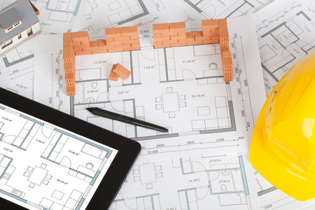 Model house construction with brick on blueprint, helmet and tabletの写真素材