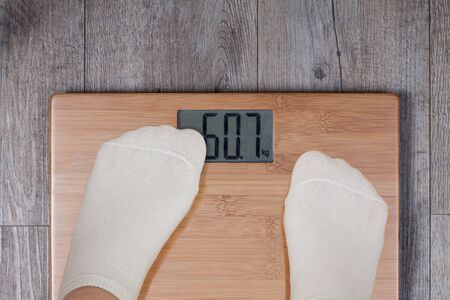 Legs of woman standing on weight scale and his thumb covering display. Funny weight concept.の写真素材