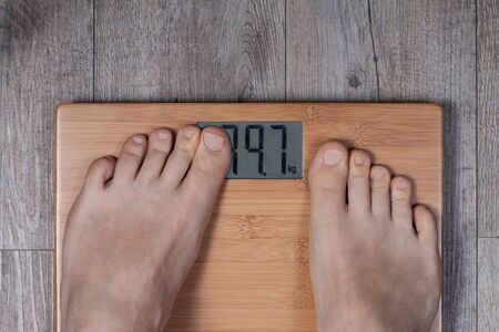 Legs of man standing on weight scale and his thumb covering display. Funny weight concept.の写真素材