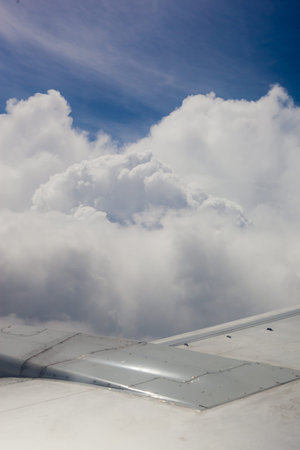 Plane wing, ground, clouds and sky