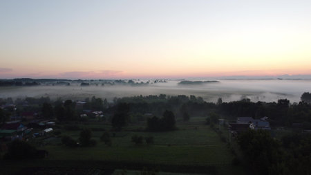 Aerial view of village in fig with golden sunbeams at sunrise in summerの写真素材