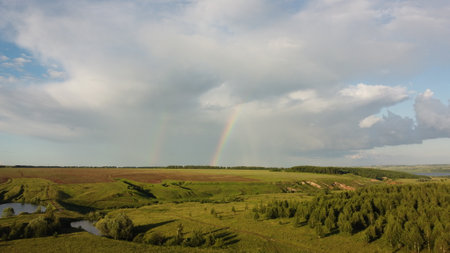 The sky with a rainbow over a meadow rural landscape. View from the heightの写真素材