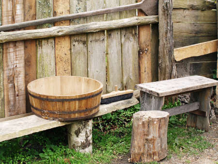 Old wooden bowl and bench against wooden fence, traditional wooden equipment の写真素材