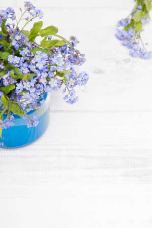 small blue flowers in a jar on a white wooden backgroundの写真素材