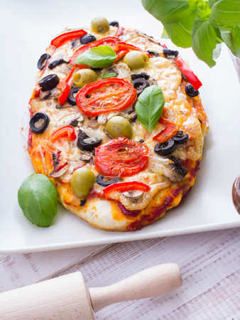 pizza with tomatoes, mushrooms, olives and peppers served on a plate on a wooden tableの写真素材