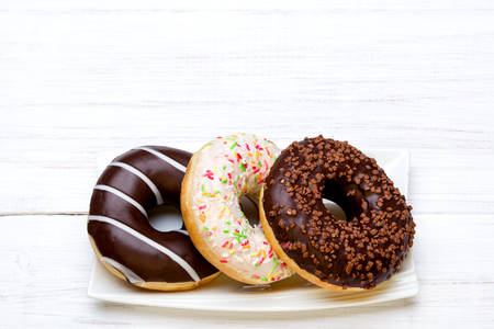 Tasty donuts with icing and chocolate on white wooden background, copy spaceの写真素材
