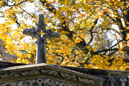 Old stone memorial cross at cemetery. Religious Christian symbol on autumn trees background