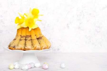 Tasty Easter Cake, easter eggs and daffodil flowers on white wooden background, copy space