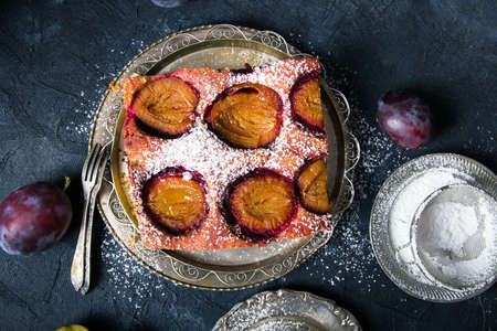 Tasty plum cake with pieces of fruit and powdered sugar on a dark backgroundの写真素材