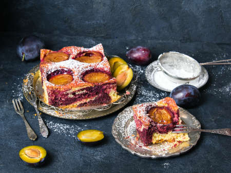 Tasty plum cake with pieces of fruit and powdered sugar on a dark backgroundの写真素材