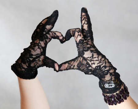 Two young woman forms heart shape with  theirs hands. They are wearing sexy black lacy gloves.の写真素材