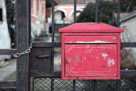 Old, red mailbox in a metal gate in front of a garden の写真素材