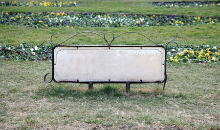 Empty information table in a park surrounded by grass and flowers behind it の写真素材