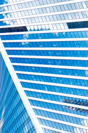Abstract skyscrapers with reflection in windows blue sky, white clouds and sun glare