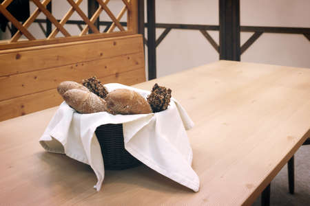 Wicker basket with bread. Bread and buns inside basket. Fresh bakery products on table. Tastes best when warm.の写真素材