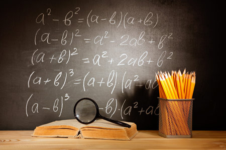Old schoolbooks magnifier and pencils lying on a wooden school desk in front of a black chalkboard...