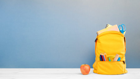 Backpack with different colorful stationery and apple on table and blue background. Banner design...